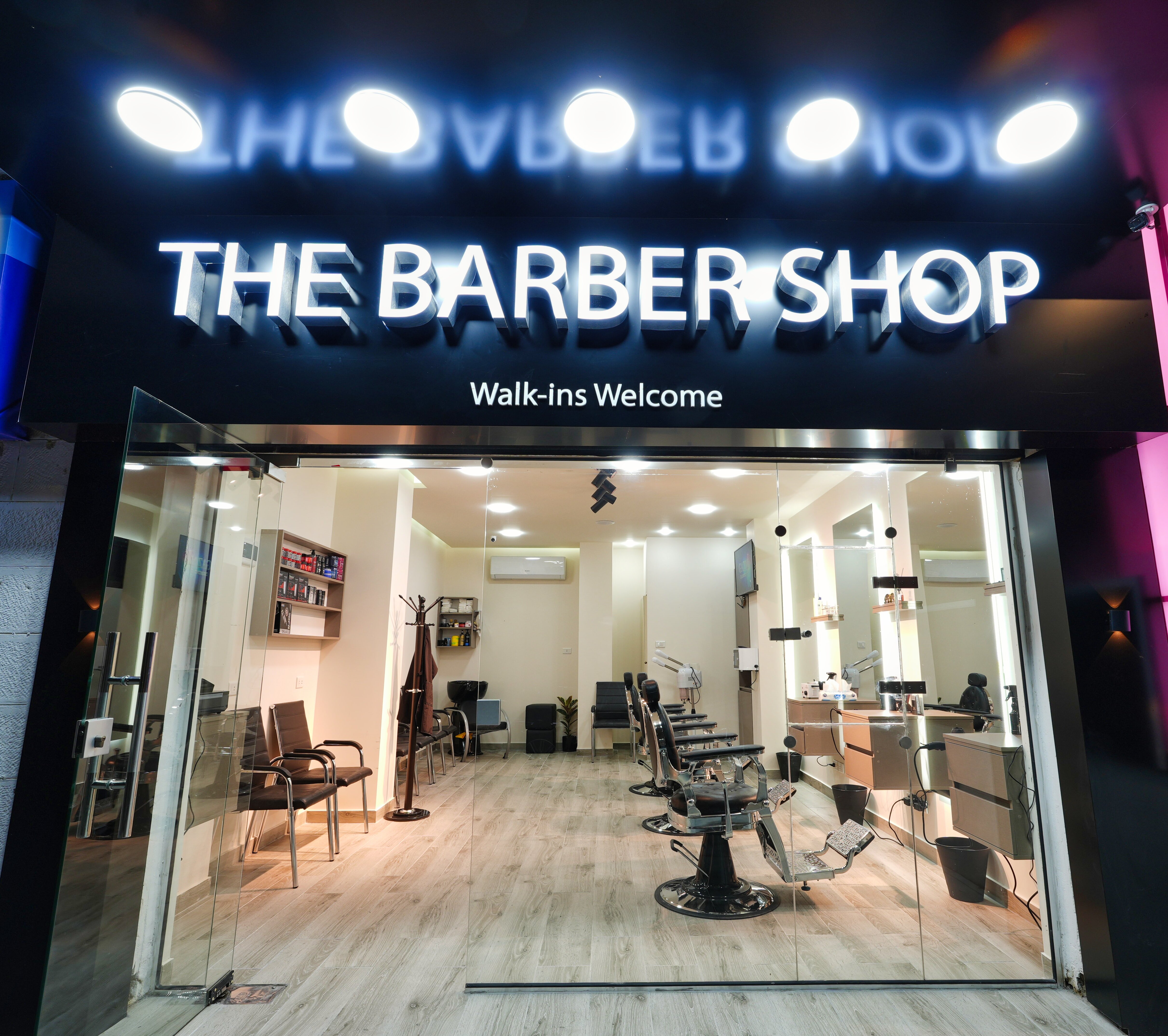 The Barber Shop illuminated storefront sign at night with the shop interior visible through the glass