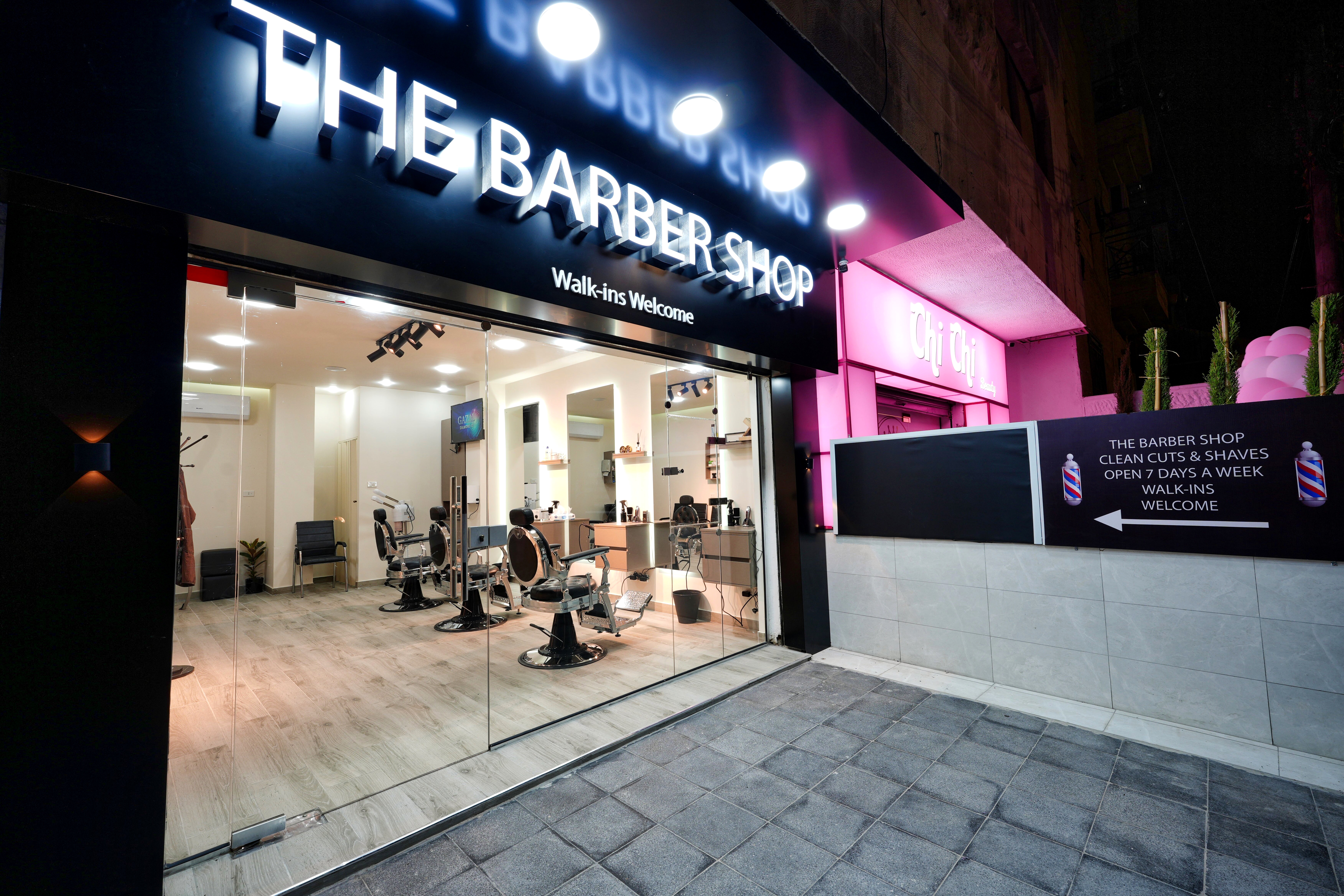 The Barber Shop storefront lit up at night, with a sidewalk sign reading Clean Cuts & Shaves