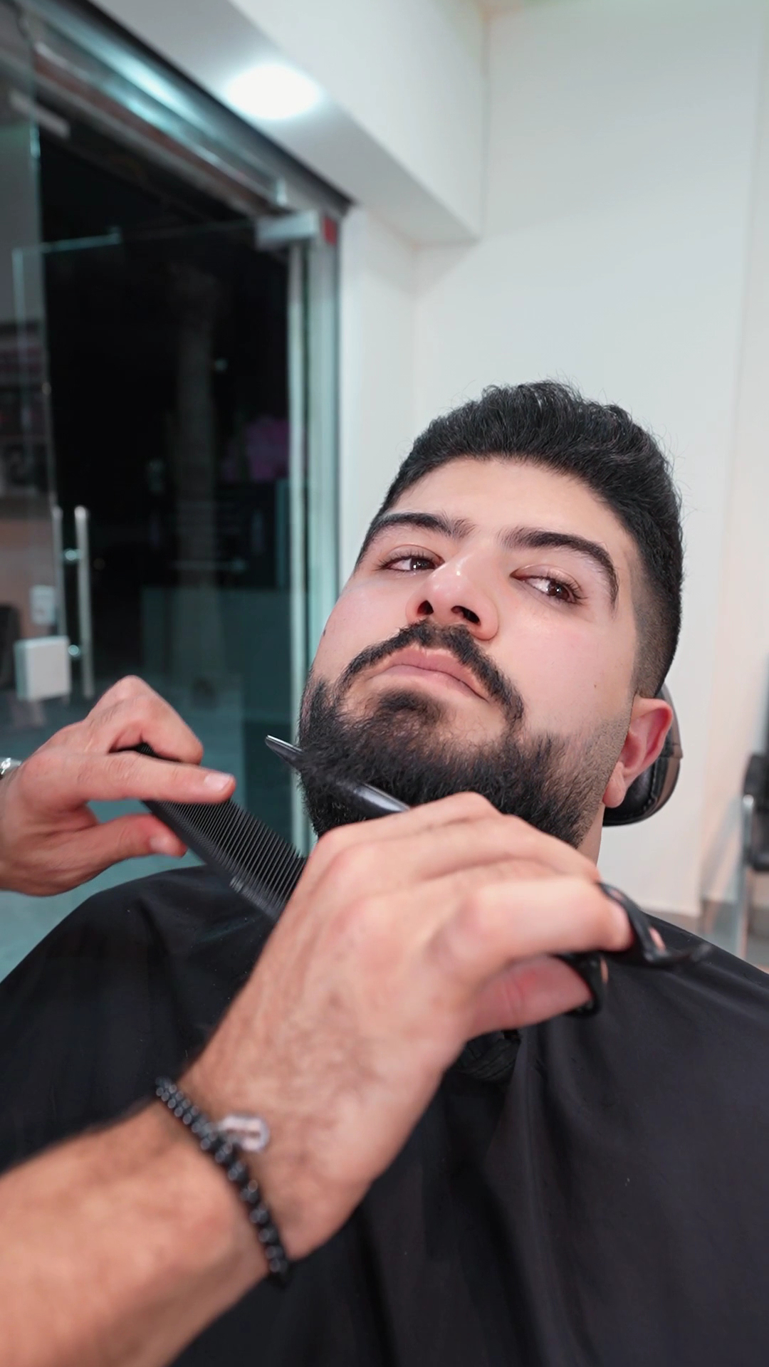 Barber trimming a client's beard with a comb and scissors